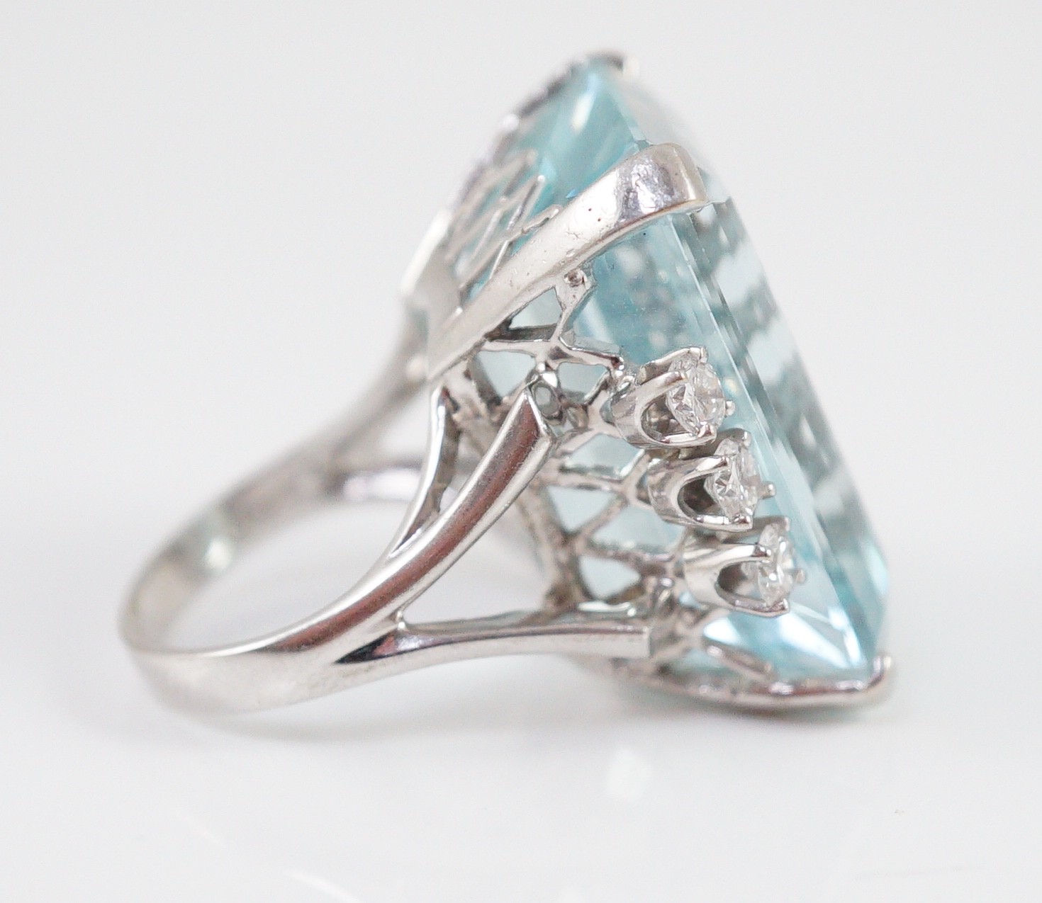 A large modern 14k white gold and emerald cut aquamarine set dress ring, flanked by six round cut diamonds
